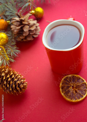 red cup with hot tea on a red background with dried orange and cones. Christmas card.