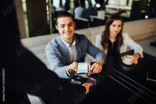 Portrait of couple sitting at table in restaurant while man paying for dinner by credit card and phone for waitress.