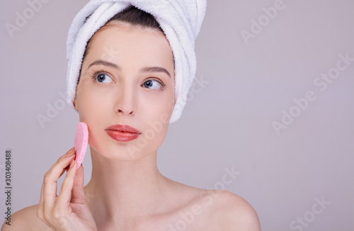 A pensive brunette cleans her face with a sponge.