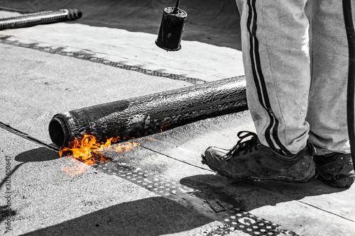 repair of bitumen roof with roll surfacing material with fire gas burner close-up, front and background blurred with bokeh effect
