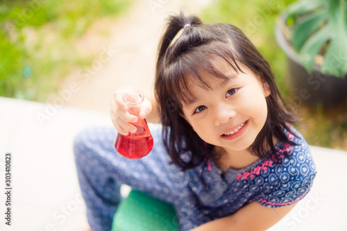 Happy Little scientist asian girl with red liquid into flask on white background. Home school girl learning about science and pouring reagent into flask.Chemistry class at home.