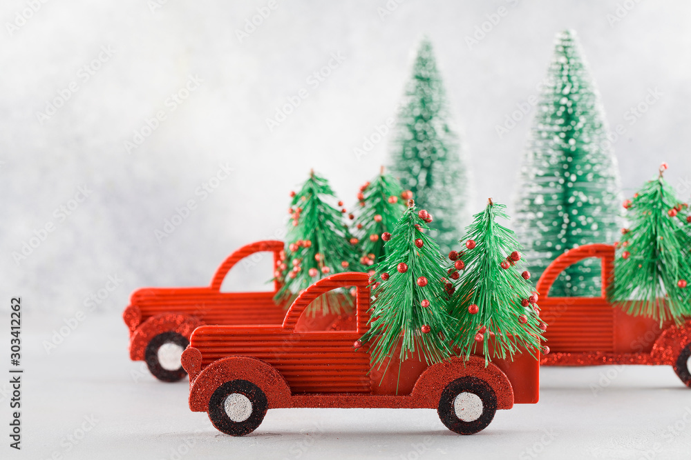 Small toy cars carring christmas tree on blue background . Sesonal holidays, greeting card, christmas mood concept.