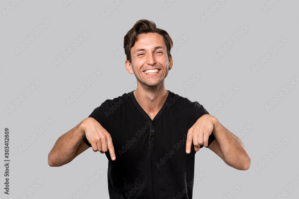 Smiling man in a black tee shirt pointing with finger down. Copy space for advertising Smiling man in a black tee shirt pointing with finger down. Copy space for advertising