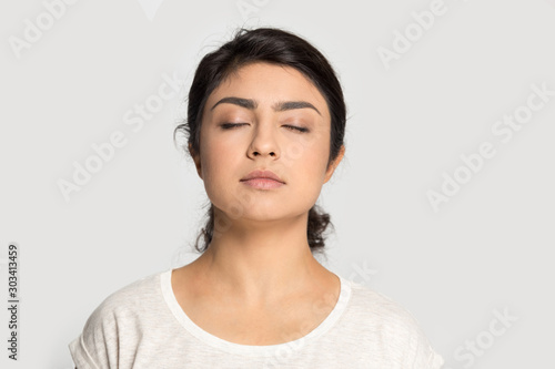 Calm Indian girl with closed eyes breathing deep, meditating