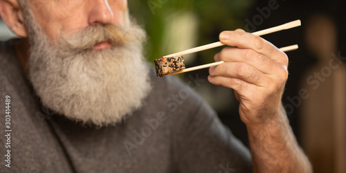 Bearded senior man eating sushi at home.
