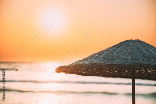 Close Up Umbrella On Sandy Beach. Sun Sunshine Above Wicker Umbrella At Summer Sunrise Sunset