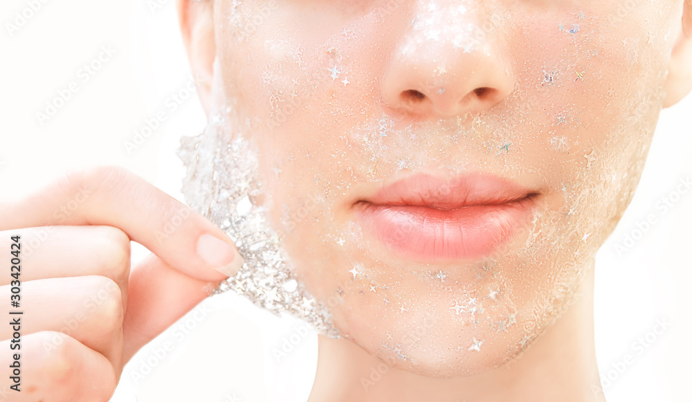 Φωτογραφία Beautiful young woman with healthy skin removes purifying transparent peel off mask with shiny sparkling star glitter from her face