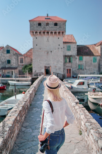 Photography and travel. Young woman walking with her camera near Kastel Gomilica Castle on Dalmatia coast, Croatia.