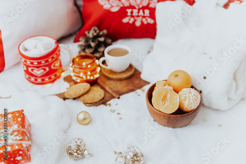 Christmas cozy composition. Winter holiday concept. Cup with coffee, tangerines, cookies, and decorations on the bed