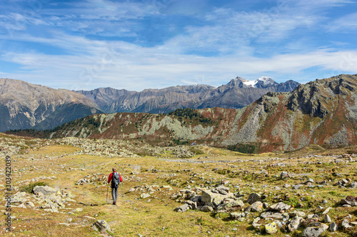 Rear view of a male hiker in autumn walking in the Tyrolean Alps, Austria. Landscape with grass, rocky mountains and blue sky