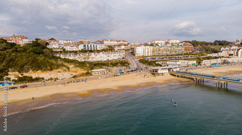 An aerial view of the Boscombe Beach with sandy beach, calm flat water and pier under a cloudy sky with some blue sky