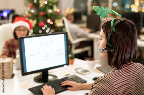 Female operator in xmas headband and headset sitting in front of computer screen