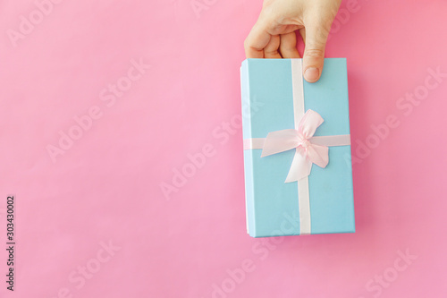 Simply design female woman hand holding blue gift box isolated on pink pastel colorful trendy background. Christmas New Year birthday valentine celebration present romantic concept. Copy space photo