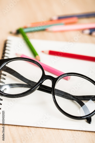 Reading eyeglasses on table with book and color pencil close up