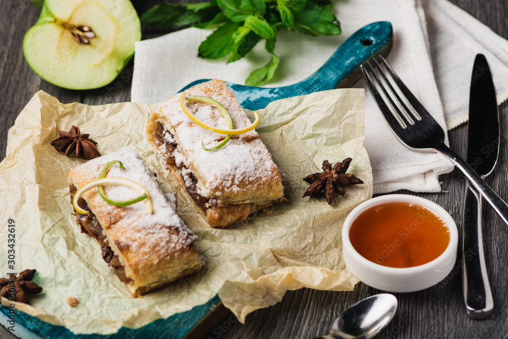 Homemade apple strudel on baked paper, served with honey on the blue wood board