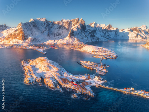 Aerial view of small islands and bridge over the sea and snowy mountains in Lofoten Islands, Norway. Hamnoy at sunrise in winter. landscape with blue water, rocks, buildings, rorbu and road. Top view