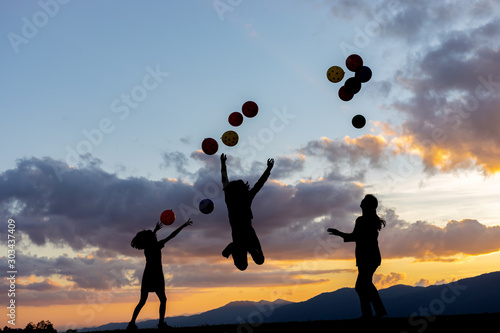 Silhouette happy family playing with colorful balloons on mountain park at summer sunset, summer holidays concept