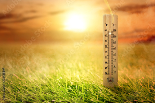 Thermometer with high temperature on the meadow with glowing sun background photo