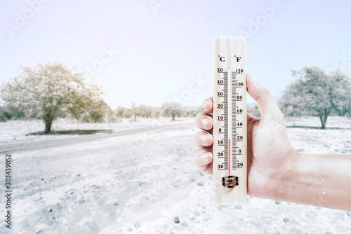 Hand holding thermometer measuring the temperature outdoor with a clear sky background