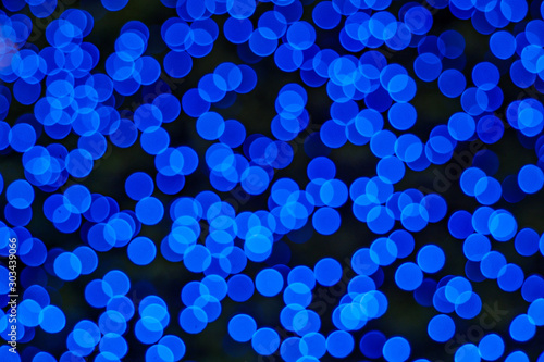 Illuminated Abstract round deep blue bokeh on dark background. Colourful glitter bokeh from out of focus view of decoration bulbs. © Peeradontax
