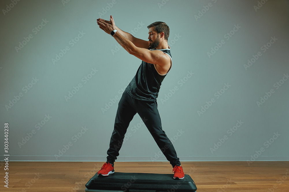muscular young man training on step platforms on the gray background in the studio