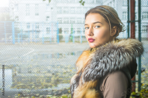 Beautiful caucasian girl in winter clothes walk on the street, in a urban background, with autumanl foliage and a confident expression