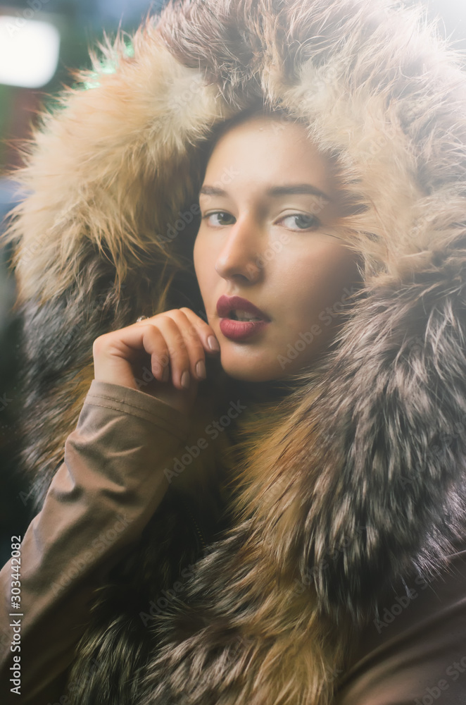 Beautiful caucasian girl in winter clothes on the street, attractive teenager portrait with a fur jacket and a self confident expression, she's illuminated with a white bulb panel Beautiful caucasian girl in winter clothes on the street, attractive teenager portrait with a fur jacket and a self confident expression, she's illuminated with a white bulb panel