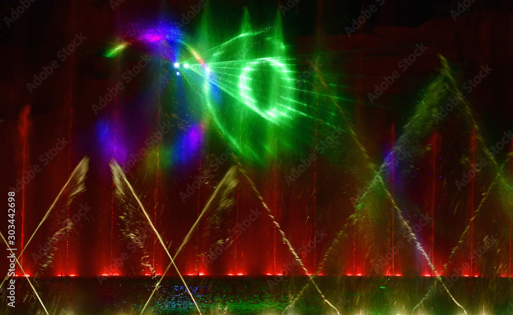 Colorful water fountains. Beautiful laser and fountain show. Large multi colored decorative dancing water jet led light fountain show at night. Dark background. Colorful water fountains. Beautiful laser and fountain show. Large multi colored decorative dancing water jet led light fountain show at night. Dark background.