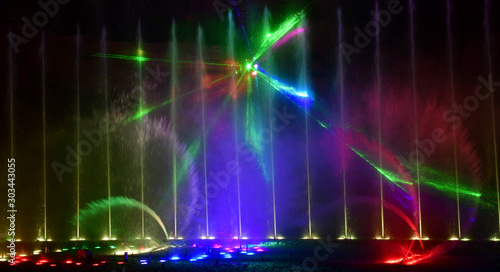 Colorful water fountains. Beautiful laser and fountain show. Large multi colored decorative dancing water jet led light fountain show at night. Dark background.