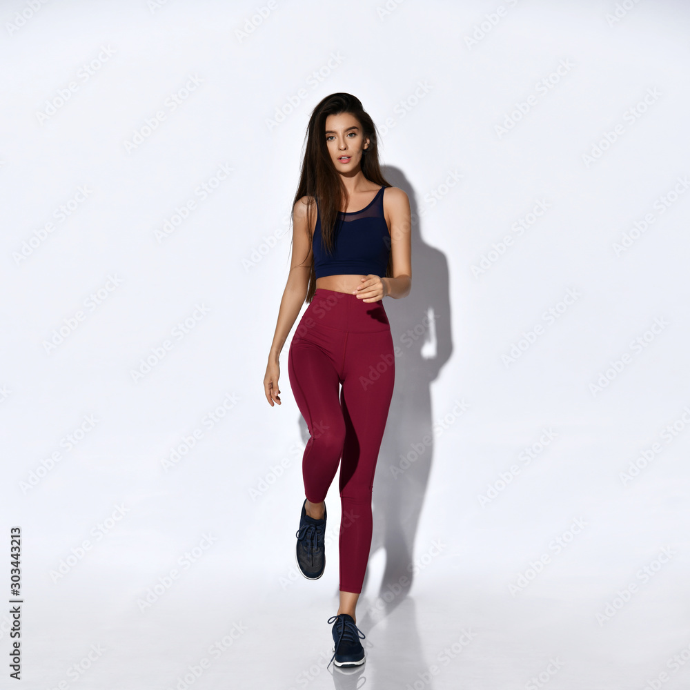 Sporty woman runner walking or running on light gray background. Attractive girl in modern fashionable sportswear Sporty woman runner walking or running on light gray background. Attractive girl in modern fashionable sportswear