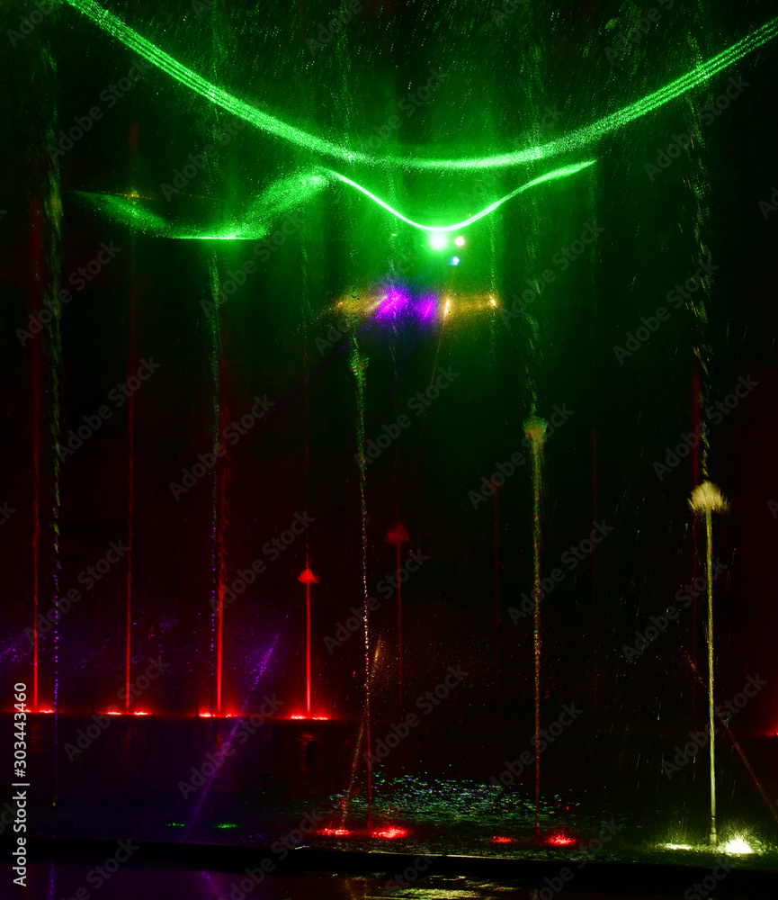 Fototapeta premium Colorful water fountains. Beautiful laser and fountain show. Large multi colored decorative dancing water jet led light fountain show at night. Dark background.