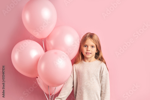 Portrait of attractive girl kid with pink air balloons isolated over pink background. Child with lon hair in white blouse look at camera
