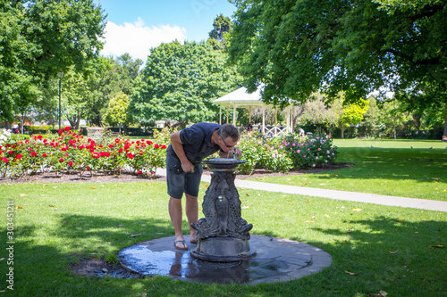 A male tourist stops in a city park to have a drink of cold water at a drinking fountain photo