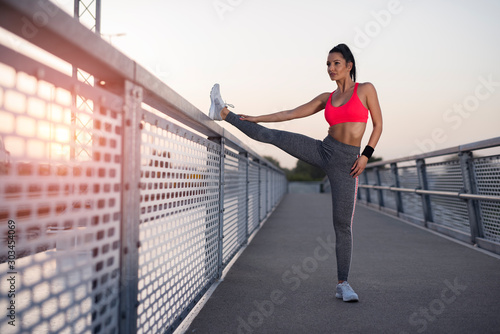 Attractive fit female, stretching leg before run on the bridge 