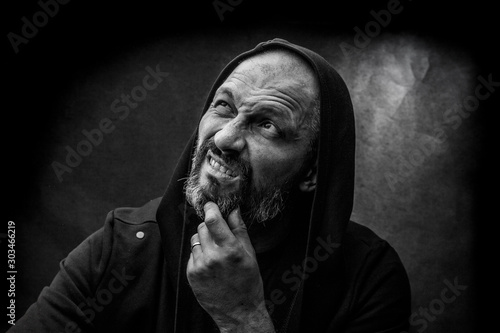 Black and white portrait of a bald bearded man in a hood on a dirty gray background. Man recalls.