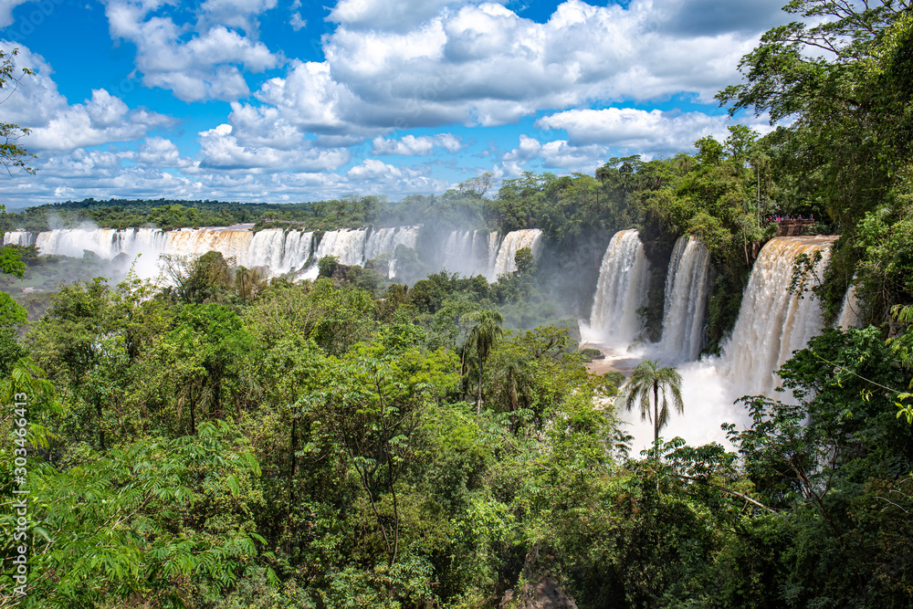 Panoramic view to waterfalls and lush green vegetation with blue sky and white clouds, Iguazu Falls, Argentina