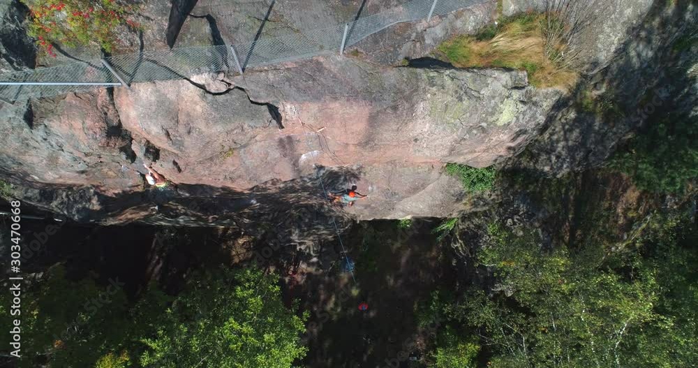 Aerial, top down, drone shot rising above a man climbing on a steep mountain wall, on a sunny day, at Naulakallio, in Mellunmaki, Helsinki, Finland Aerial, top down, drone shot rising above a man climbing on a steep mountain wall, on a sunny day, at Naulakallio, in Mellunmaki, Helsinki, Finland