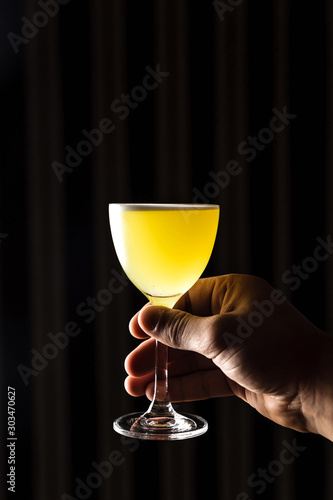 A yellow cocktail in a nick and nora glass garnished with cilantro at the bar