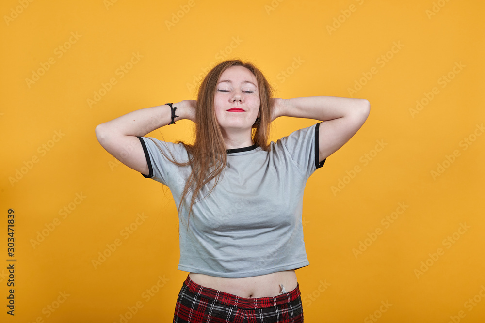 Relaxed young woman in casual clothes keeping eyes closed, with hands behind head isolated on orange wall background in studio. People sincere emotions, lifestyle concept. Relaxed young woman in casual clothes keeping eyes closed, with hands behind head isolated on orange wall background in studio. People sincere emotions, lifestyle concept.