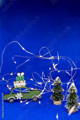 Toy car with Christmas tree and gift on roof.blue Background with garland. New Year and Christmas holiday concept.New Year festive background, vintage toys,Christmas tree on dark blue background with