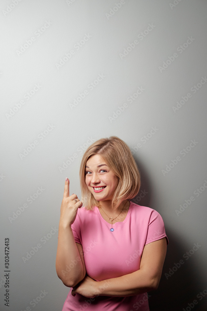 Copy space for idea. Attractive young blond woman pointing up against grey wall. Copy space for idea. Attractive young blond woman pointing up against grey wall.