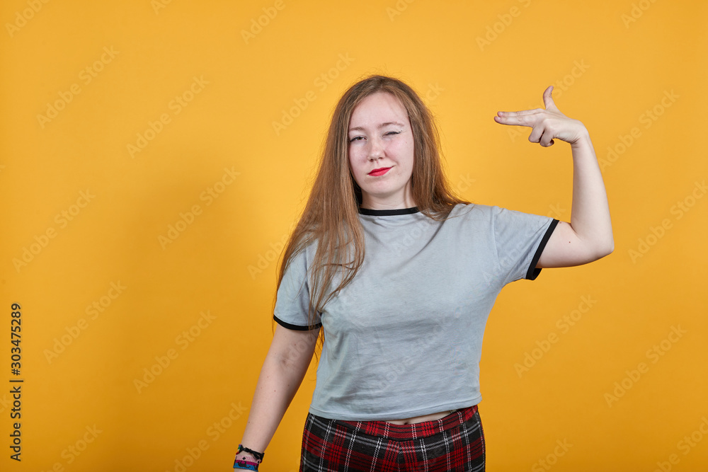 Pretty young caucasian woman in gray clothes posing isolated on orange background. People lifestyle concept. Point fingers to head as if she about shoot herself, having rainbow bracelet on hand Pretty young caucasian woman in gray clothes posing isolated on orange background. People lifestyle concept. Point fingers to head as if she about shoot herself, having rainbow bracelet on hand
