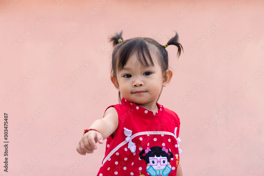 Portrait image of baby 1-2 years old. Happy Asian child girl smiling and pointing her index fingers. She wearing a red clothes. Raise hand. Learning and development of kid concept. Portrait image of baby 1-2 years old. Happy Asian child girl smiling and pointing her index fingers. She wearing a red clothes. Raise hand. Learning and development of kid concept.