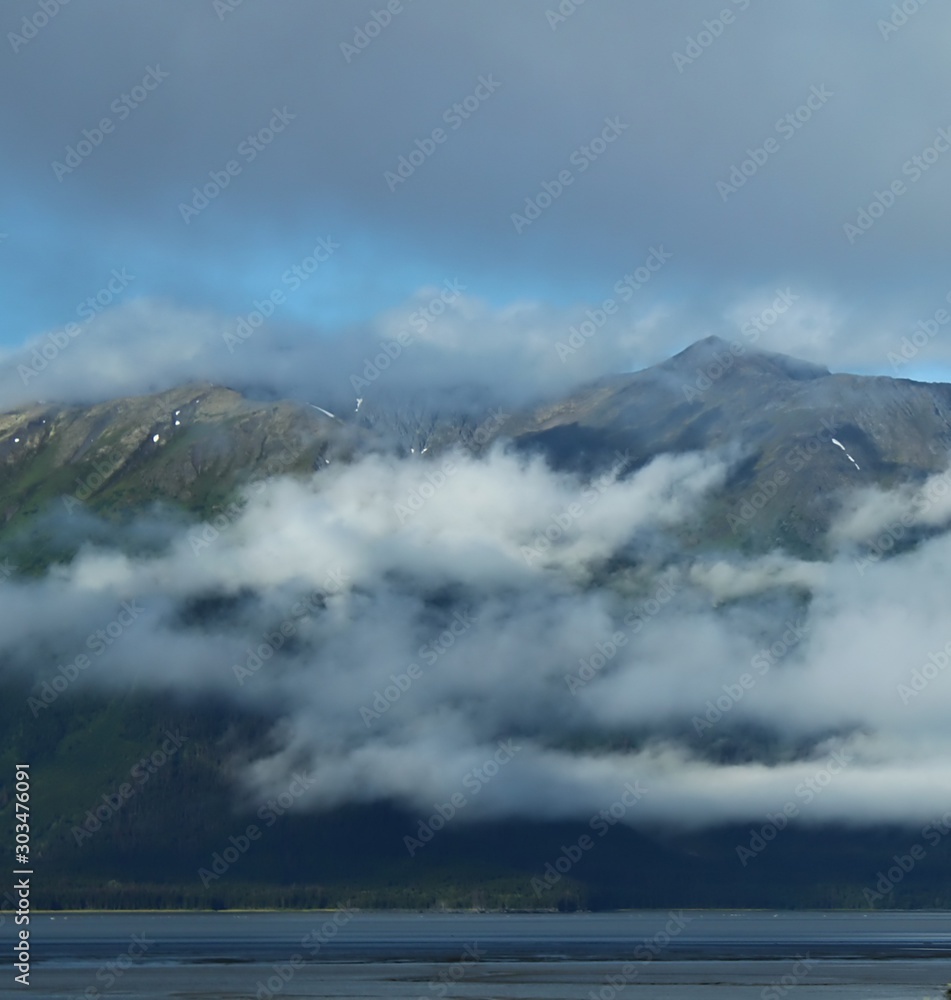 Hazy Day Clouds Hang Over The Water Front Partially Hiding Alaska Mountains.  