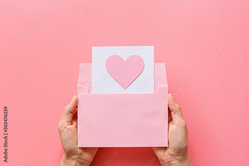 Valentine's day background. Female hands holding greeting card with pink hearth in envelope. Flat lay, top view, mockup, template, copy space. Minimal abstract composition for 14 February celebration Valentine's day background. Female hands holding greeting card with pink hearth in envelope. Flat lay, top view, mockup, template, copy space. Minimal abstract composition for 14 February celebration