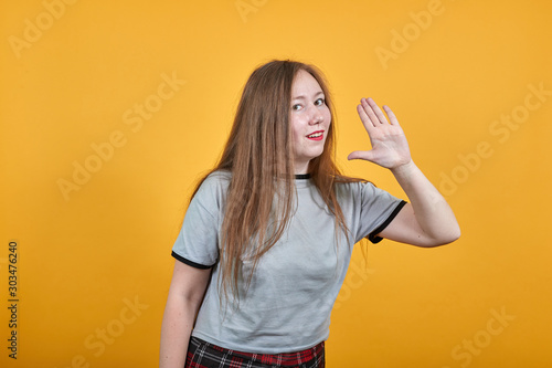 Attractive young caucasian woman shouting and announcing something, keeping hand near cheek on isolated orange background wearing nice fasion shirt
