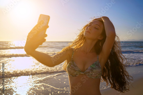Young women taking selfie photo using smartphone camera and having fun on the sunset beach