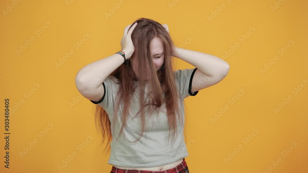 Attractive young pretty woman wearing nice gray shirt and with nice haircut,looking frustrated and takes hands on head, having rainbow bracelet over isolated orange background Attractive young pretty woman wearing nice gray shirt and with nice haircut,looking frustrated and takes hands on head, having rainbow bracelet over isolated orange background