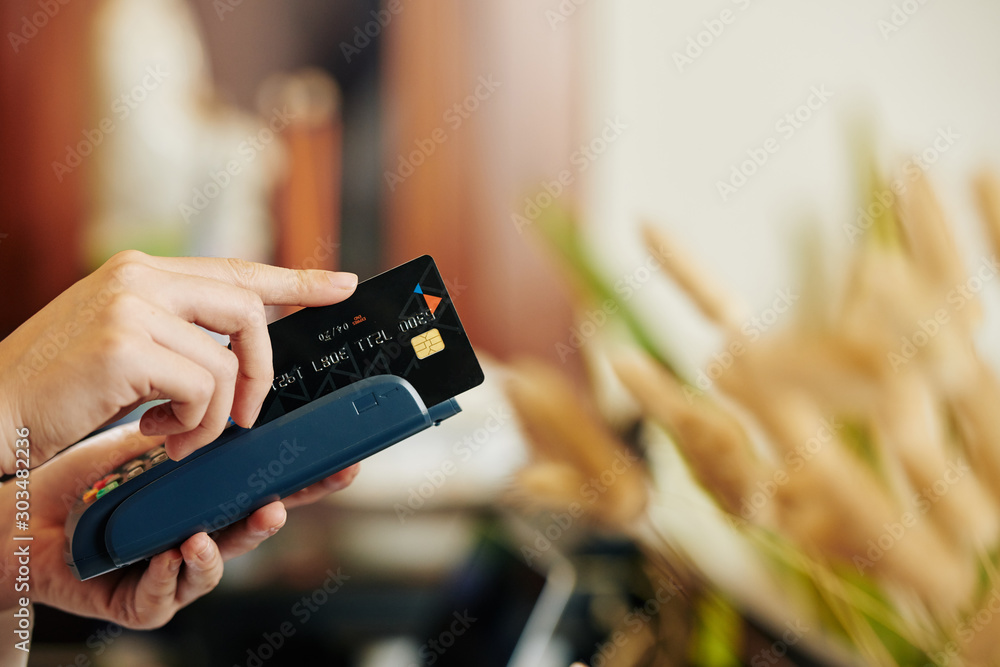 Φωτογραφία Hands of cashier swiping credit card through terminal when accepting payment fro