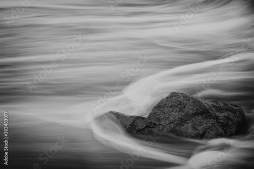 Black and white photography of sea waves in slow motion splashing into a stone. Copy space